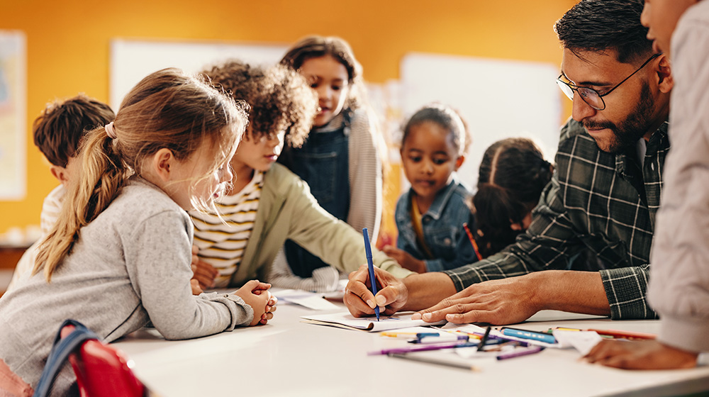 /unimagdeburg_media/Presse/Bilder/Pressemitteilungen/2024/Junge+Schuelerinnen+und+Schueler+umringt+an+einem+Tisch_+w%C3%A4hrend+der+Lehrer+etwas+schreibt+%28c%29+Shutterstock+Jacob+Lund-height-560-width-1000-p-111164.jpg